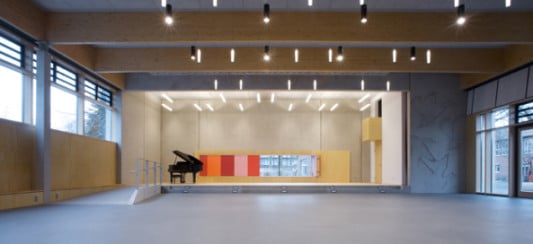 Das Holztragwerk der Halle spannt sich zwischen zwei massiven Betonkörpern, in denen auf der einen Seite die Bühne und auf der anderen die Nebenräume untergebracht sind