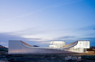 Schwungvoll geformte Rampen erheben sich wellengleich aus dem Erdboden und lassen Gebäude und Topografie miteinander verschmelzen