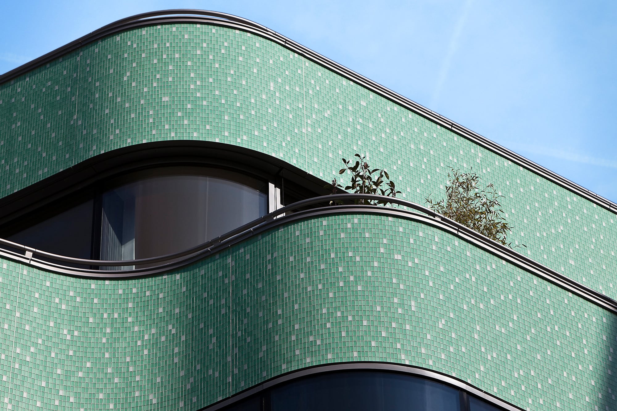 Die geschwungene Fassade ist mit einem grün-weißen Glasmosaik bedeckt