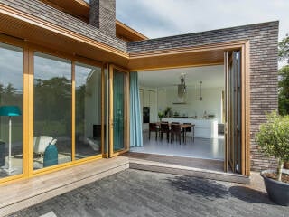 Fenstertüren werden oft als Balkon- oder Terrassentüren eingesetzt. Im Bild das Beispiel einer Glas-Faltwand mit Holzrahmen (Serie Woodline von Solarlux).