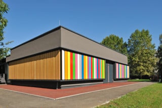 Die Fassade des Kindergartens zeigt sich in einem abwechslungsreichen Streifenmuster aus unterschiedlich gefärbten Lamellen
