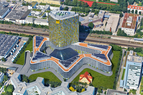 Luftbild mit Photovoltaikdächern: Das Gebäude besteht aus einem fünfgeschossigen, sternfömig geschwungenen Sockelbau mit dynamisch geformtem Innenhof sowie einem 18-geschossigen Büroturm