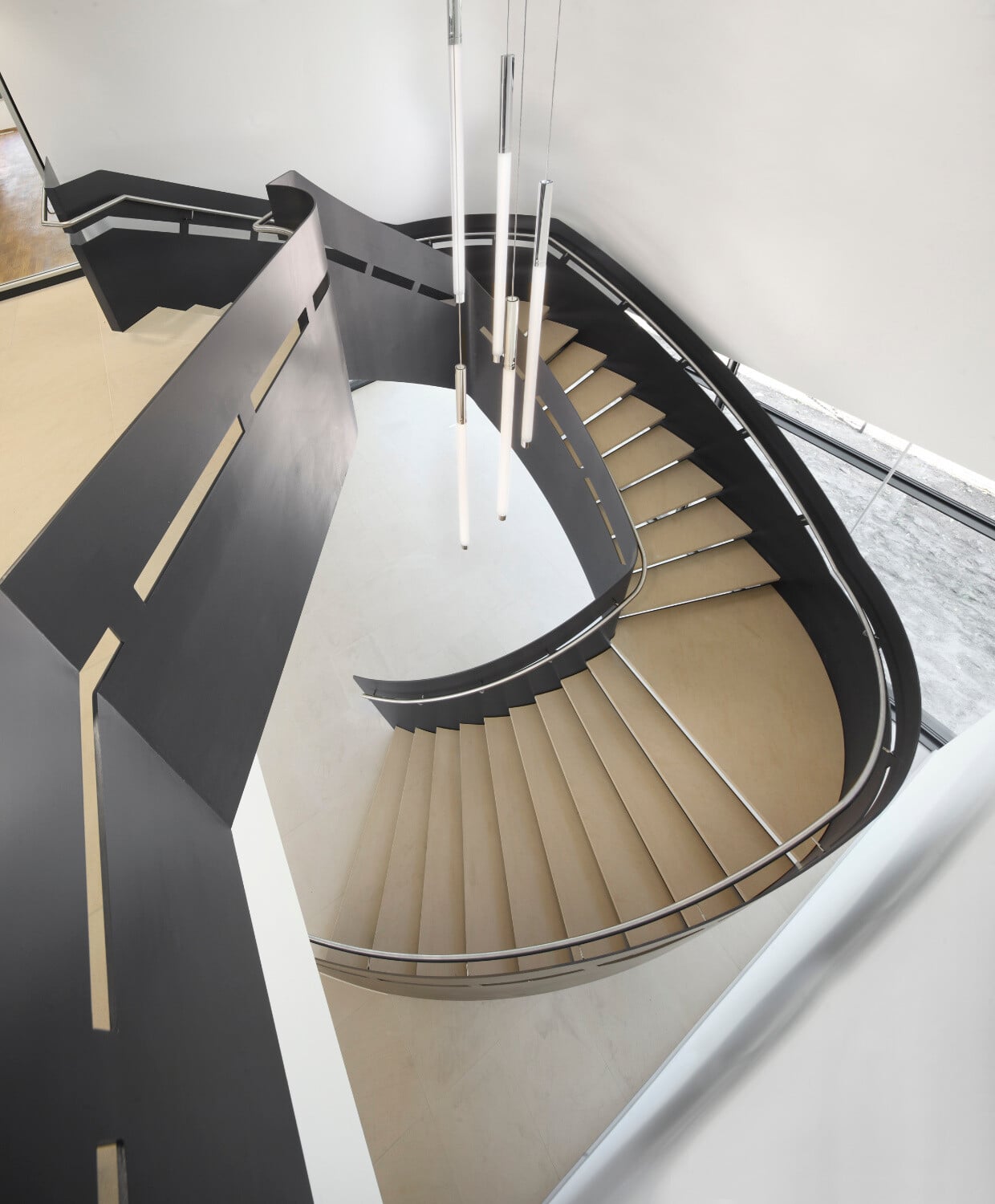 Dreiecksförmig gewendelte Stahltreppe mit Steinbelag im „Haus der Wirtschaft des Unternehmerverbands Südhessen” in Darmstadt.