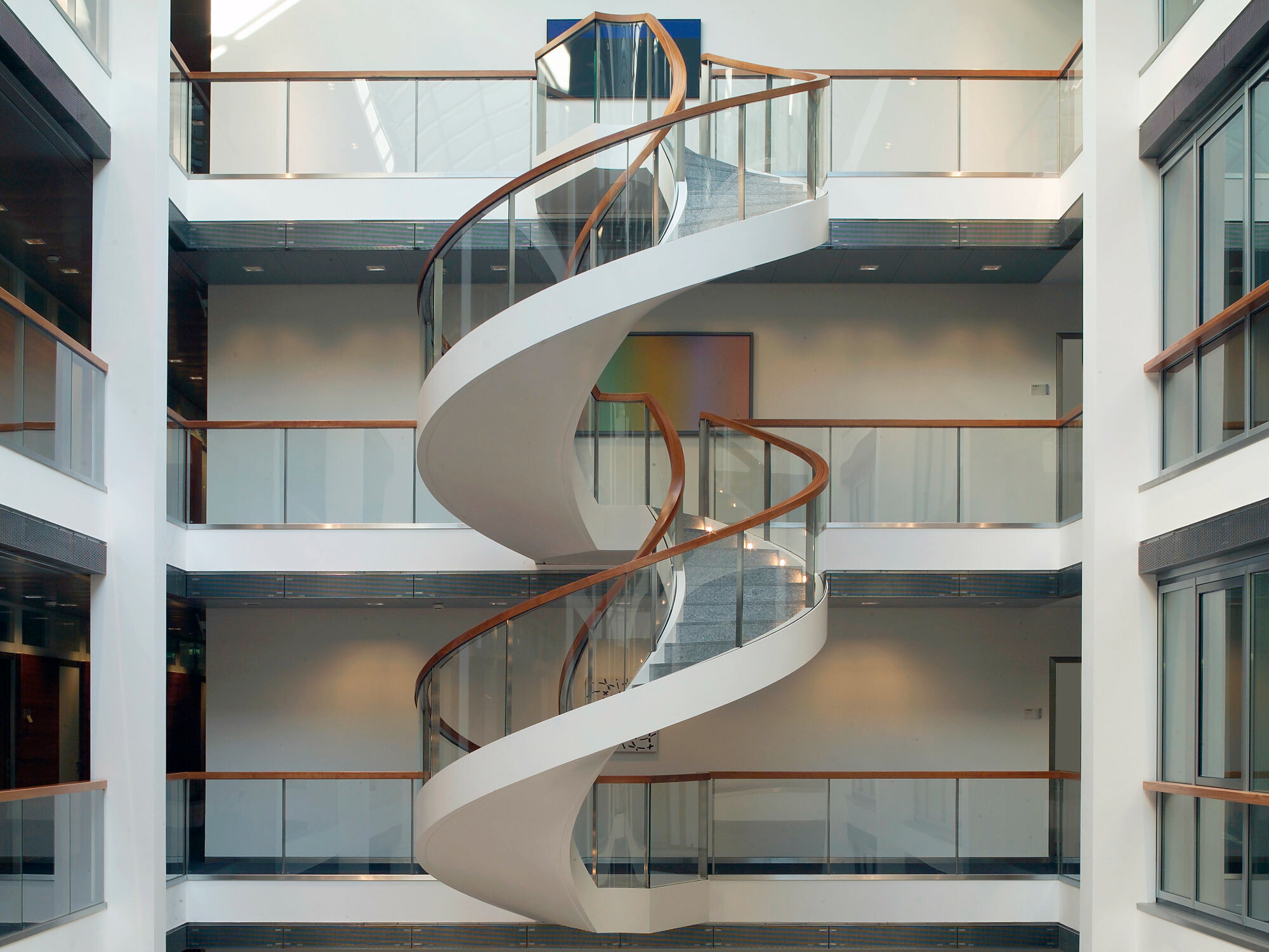 Wendeltreppe mit Glasgeländer und einer dem Treppenlauf angepassten Untersichtsverkleidung aus lackiertem Stahlblech im Foyer der KfW in Frankfurt.