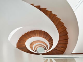 Ellipsenförmig gebogene Treppe mit Flachstahl-Brüstungswangen und Faltwerkstufen aus Holz im Seehotel Riva in Konstanz.