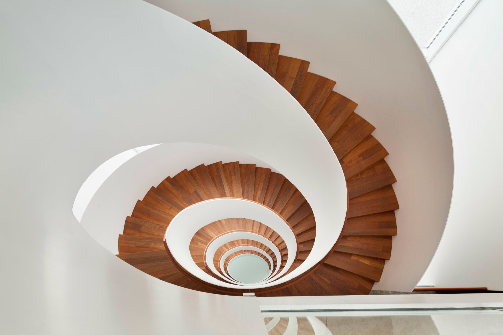 Die weiß lackierte Oberfläche der ellipsenförmig gebogenen Flachstahl-Brüstungswangen der freitragenden Treppen in Konstanz harmoniert mit den Faltwerkstufen aus Holz.