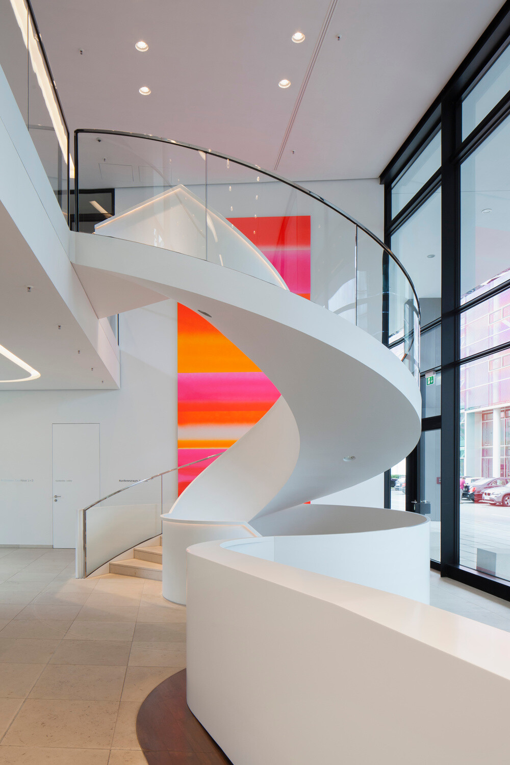 Wendeltreppe mit gebogenem Glasgeländer ohne Pfosten und einem oberen Kantenschutz aus Edelstahl-U-Profilen im Geschäftshaus Funky in München.