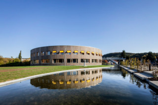 Eine Holzfassade mit Vertikalverschalung umfasst den zweigeschossigen Rundbau