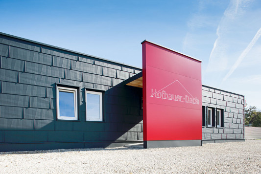 Die kleinteilige strukturierte Aluminiumfassade steht im Kontrast zur glatten Oberfläche der roten Wandscheibe