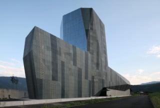 In den Fassade wechseln sich Glasflächen mit perforierten Aluminiumpaneelen in drei Grautönen ab