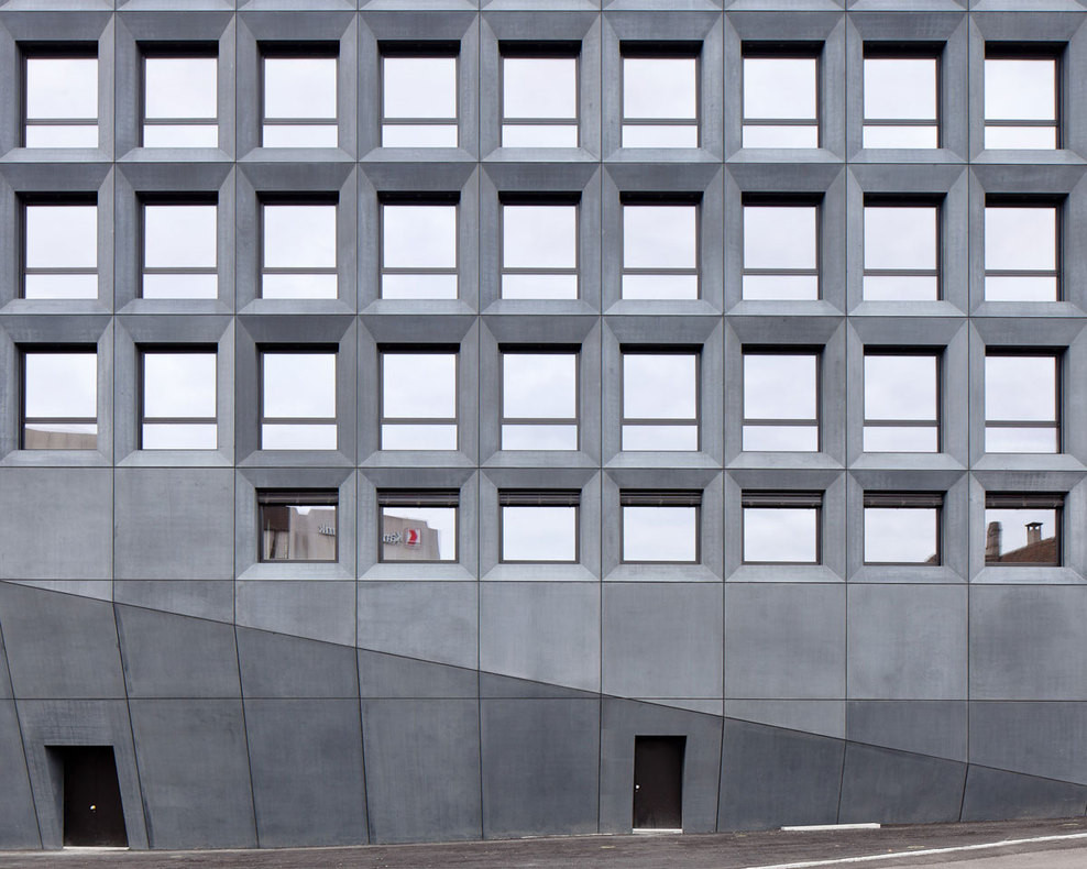 Nach unten hin verjüngt sich die streng gerasterte Betonfassade
