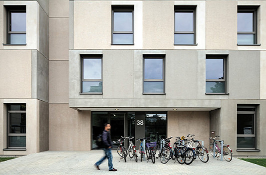 Sandgestrahlte Sichtbetonfertigteile in verschiedenen Grautönen und pro Geschoss versetzt angeordnete Fenster prägen die Wohnheime
