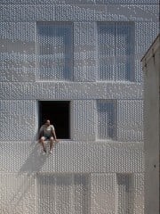 Vor der Westfassade verläuft eine Vorsatzschale aus perforierten Alu-Blechen, im Bereich der Fenster sind diese als bewegliche Paneele ausgebildet