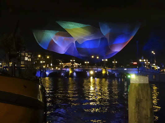 Eine filigrane, scheinbar immaterielle Form schwebt über dem Wasser der Amstel