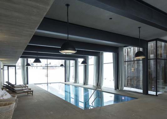Sichtbeton, Glas und Naturstein prägen das Schwimmbad mit Ausblick zur Berglandschaft