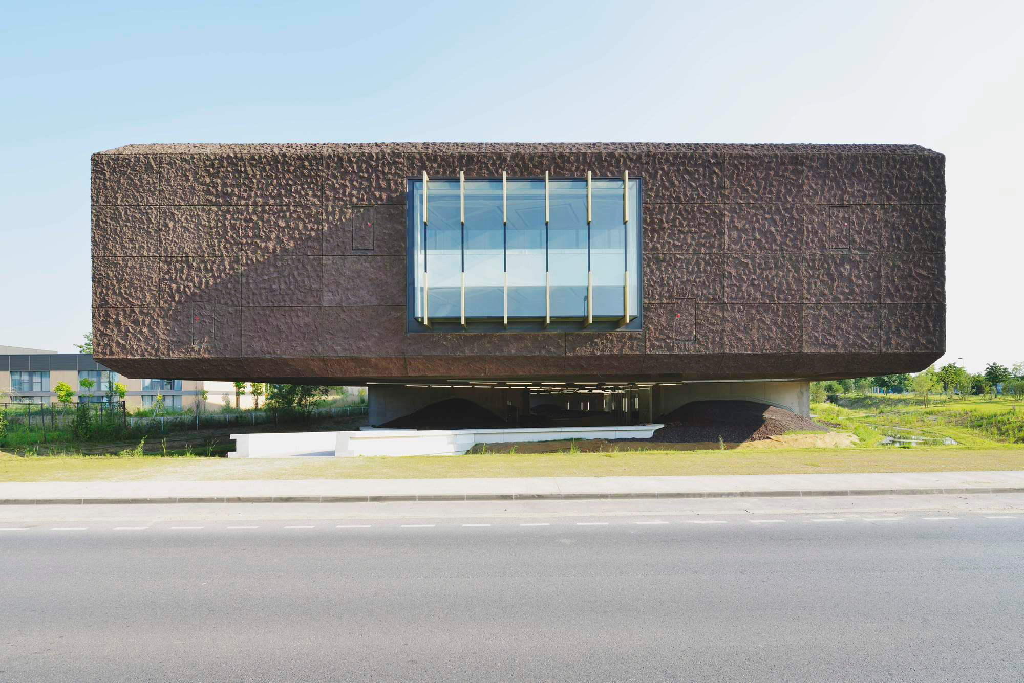 Die Fassade besteht aus dunklen, rotbraunen Betonelementen mit einem unregelmäßig gewellten Relief, durchbrochen von gläsernen Erkern