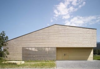 Südansicht mit der Fassade aus einer schmalen Weißtannenholzlattung (unbehandelt) und dem charakteristischen flachen Satteldach mit unterschiedlichen Neigeflächen