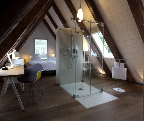 In einem offen gestalteten Gästezimmer im Dachgeschoss ist die Dusche zentral platziert