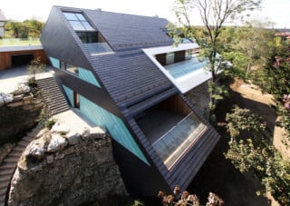 Beinahe mit der schroffen, hellen Felskante verwachsen erscheint die Villa, deren steil geneigte Schieferfassade sich dem Hangverlauf anpasst