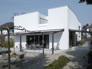 Das Wohnhaus hat mit seinen flach geneigten Dächern ein kompaktes Volumen, welches durch eine kleine Terrasse im Obergeschoss eingeschnitten wird