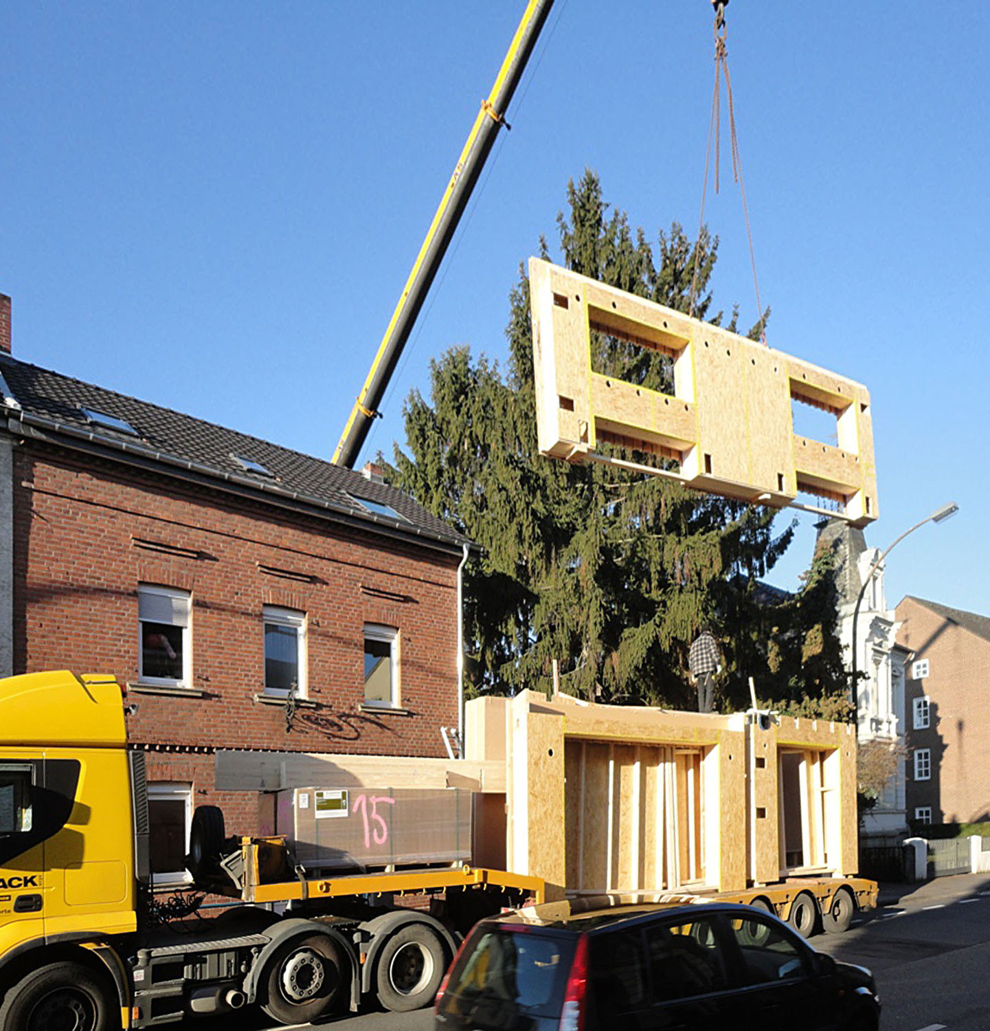 Anliefern der Holzbauelemente, die mit einem Autokran über das vordere Gebäude gehoben werden