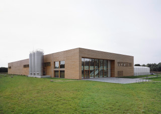 Die Nordfassade öffnet sich mit großen Verglasungen in der Lärchenlamellenfassade, dahinter befindet sich u.a. der zweigeschossige Holfladen