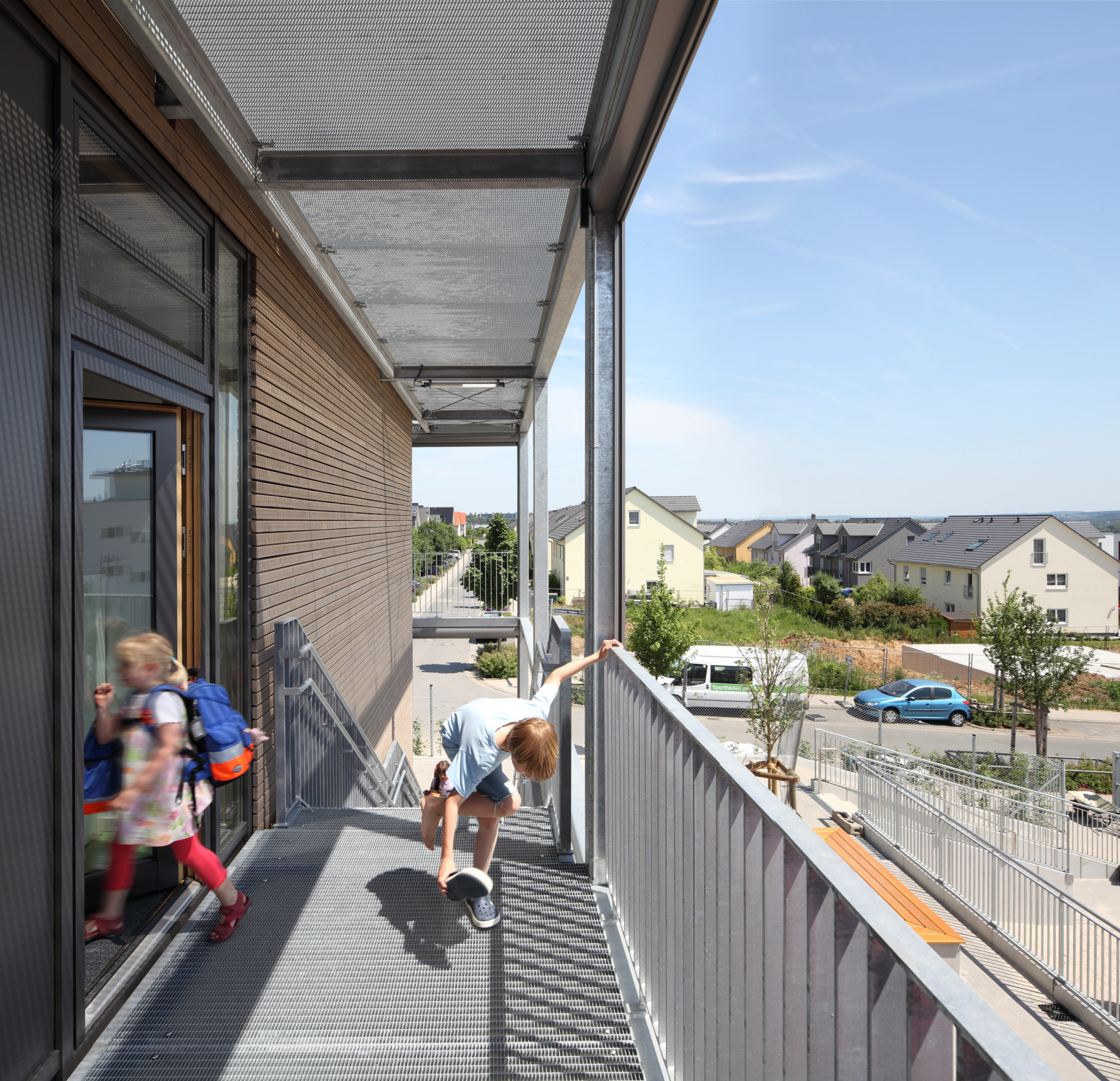 Ein umlaufender Laubengang ist über zwei Treppen mit dem Erdgeschossniveau verbunden und erfüllt gleichzeitig die erhöhten Brandschutzanforderungen an Kindertagesstätten
