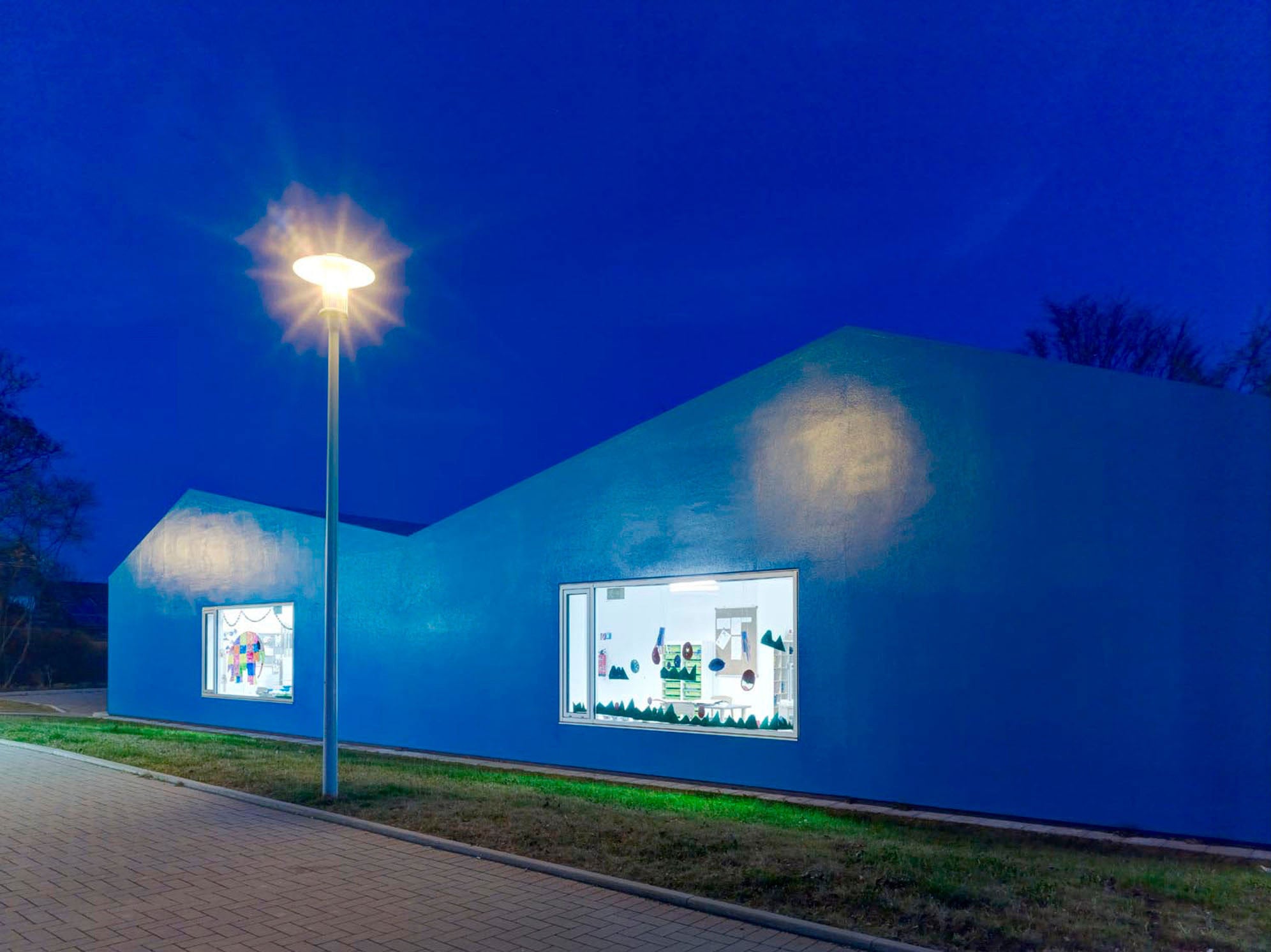 Ein einheitlich blauer Farbüberzug auf dem Dach sowie auf den geschlossenen Teilen der Außenwand unterstreicht die markante Form der Kita