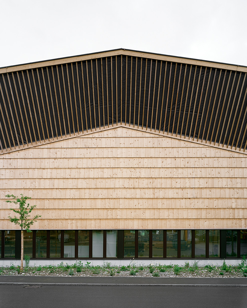Ansicht Ost: Neben der Holzschindel-Fassade ist das Gebäude geprägt durch eine markante, auskragende Dachuntersicht aus massiven Holzlatten
