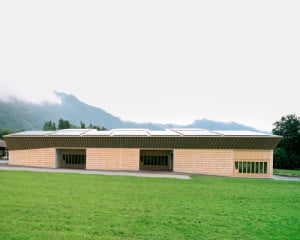 Nordansicht: Der langgestreckte Holzbau ist bekleidet mit Schindeln aus regionalem Fichtenholz