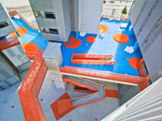 Zentrales Element ist die Verbindungsebene in zehn Meter Höhe: Mit Stegen und abgehängten Treppen gleicht sie einer Skulptur, die sich auch mit der blauen Untersicht und den hellroten Brüstungen farblich abhebt