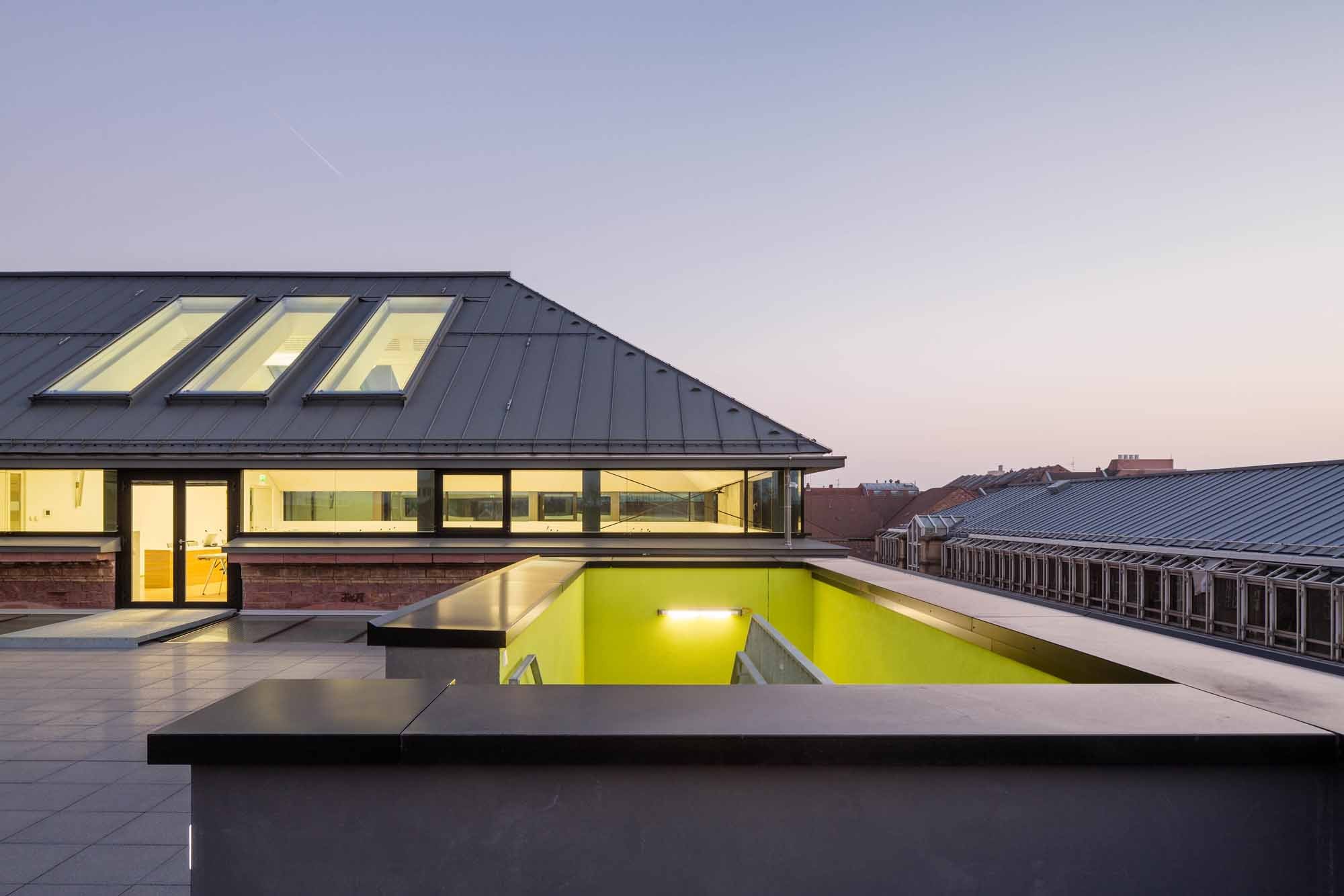 Den oberen Abschluss des Erweiterungsbau bildet eine Dachterrasse, den des Altbaus ein Walmdach; eine umlaufende gläserne Fuge trennt alt und neu