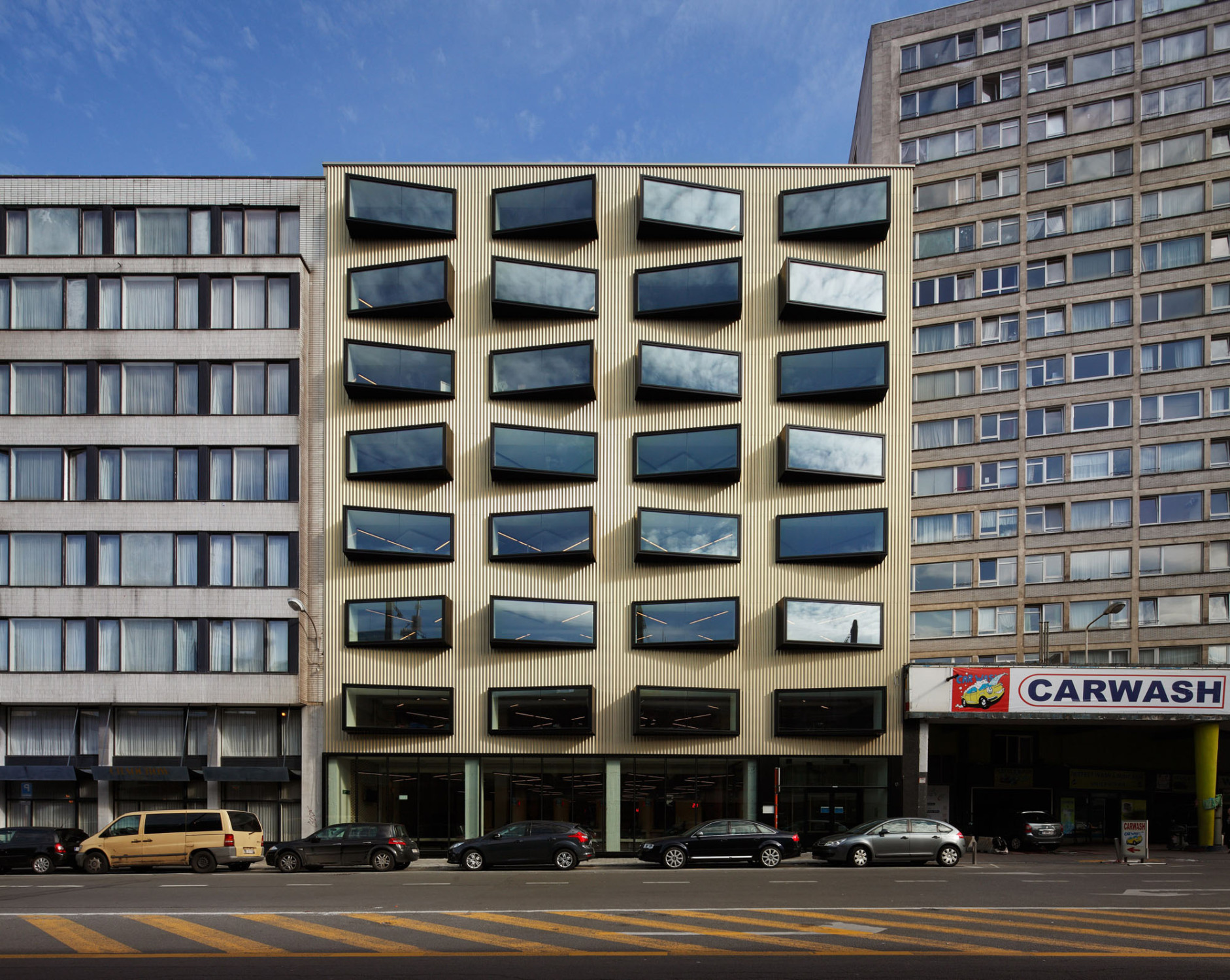 Eine champagnerfarbene, profilierte Metallbekleidung bildet die neue Fassade des Verwaltungsgebäudes, sie ist von dunklen, kastenfömigen Erkerfenstern gleichmäßig durchbrochen (Westansicht)