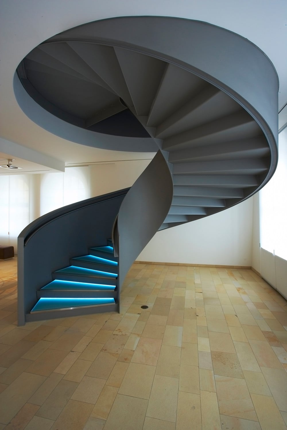 Durch die geschlossenen Brüstungen und die indirekt beleuchteten Glasstufen wird die Treppe zur Skulptur im Raum