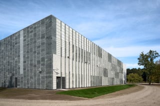 Südöstliche Gebäudeecke: Die überwiegend geschlossene Fassade ist von einem Raster aus hellen Betonfertigteilen und dunkelgrauem Naturstein überzogen, das den Eindruck dicht gereihter, gefüllter Regale vermittelt
