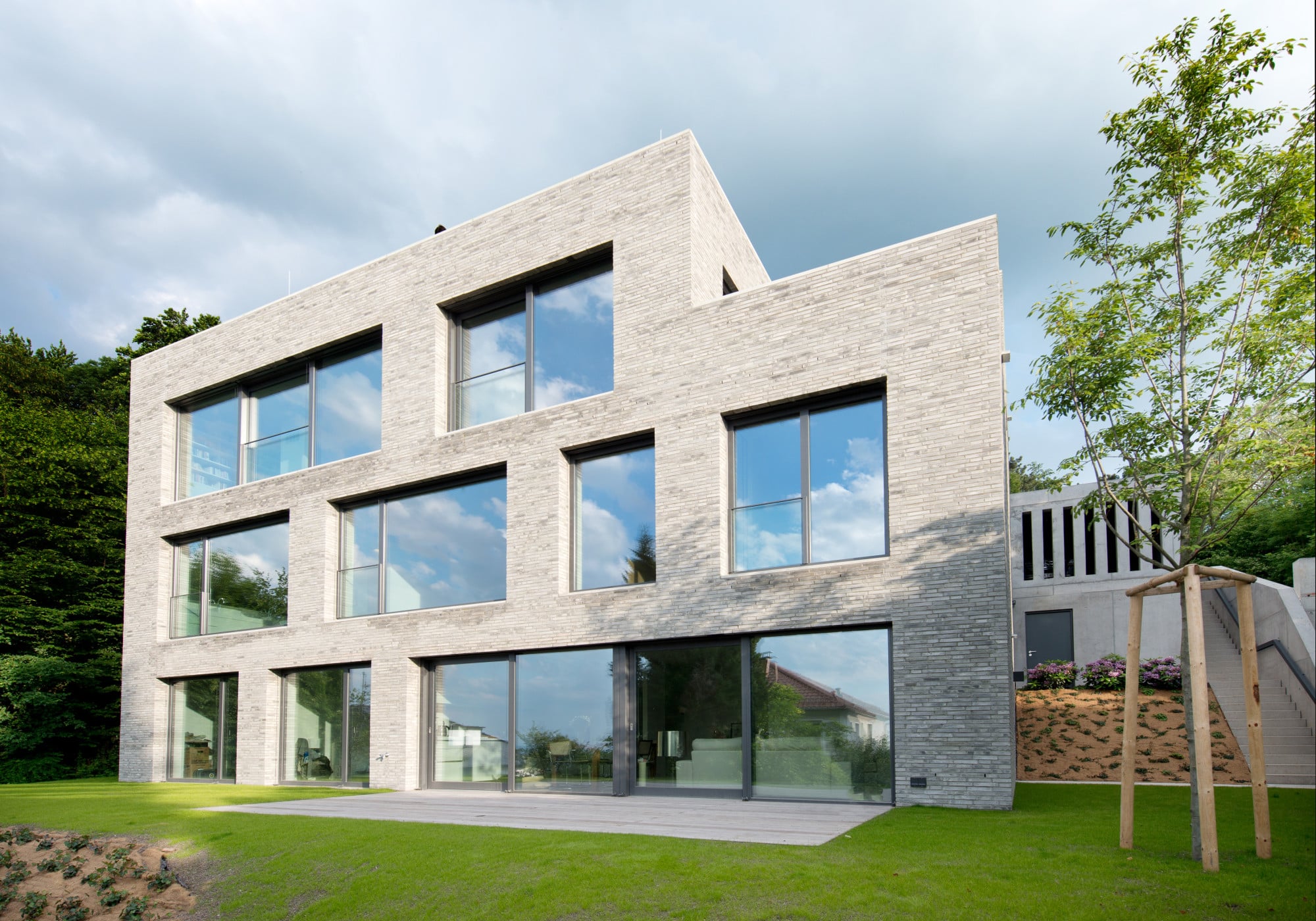Talseitig zeigt sich der dreigeschossige Baukörper in seiner gesamten Höhe mit einer durch große Fenster perforierten Mauerweksfassade aus wassergestrichenen Kohlebrandziegeln in changierenden Grautönen (Nordansicht)