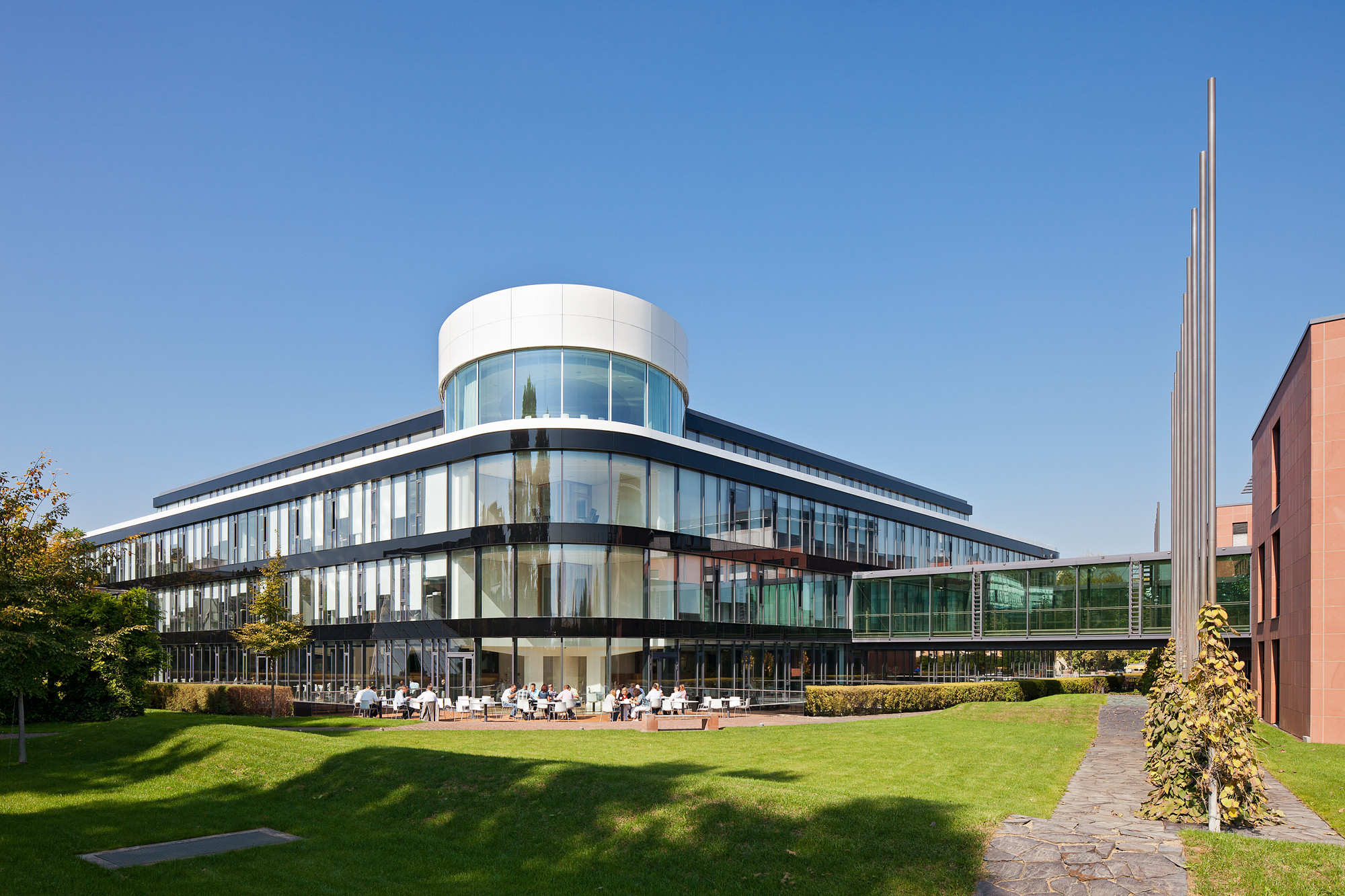 Lediglich die horizontale Ausrichtung blieb erhalten, nach der Sanierung dominiert Glas die Fassade; hinter dem weißen Zylinder im Staffelgeschoss liegt der Konferenzraum  