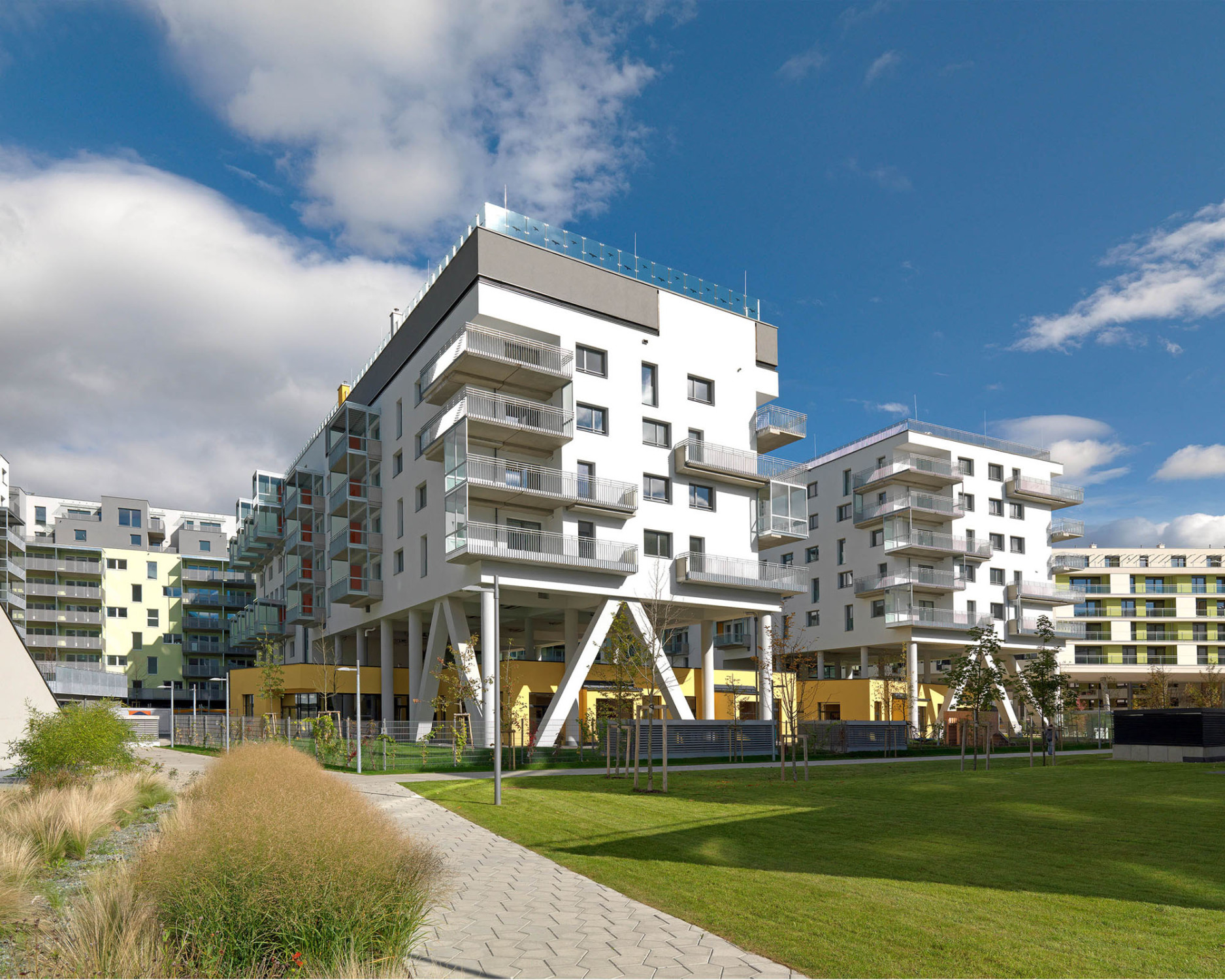 Blick in den Hof: Der gelb verputzte Kindergarten erstreckt sich unterhalb der aufgeständerten Baukörper (Ansicht Südwest)
