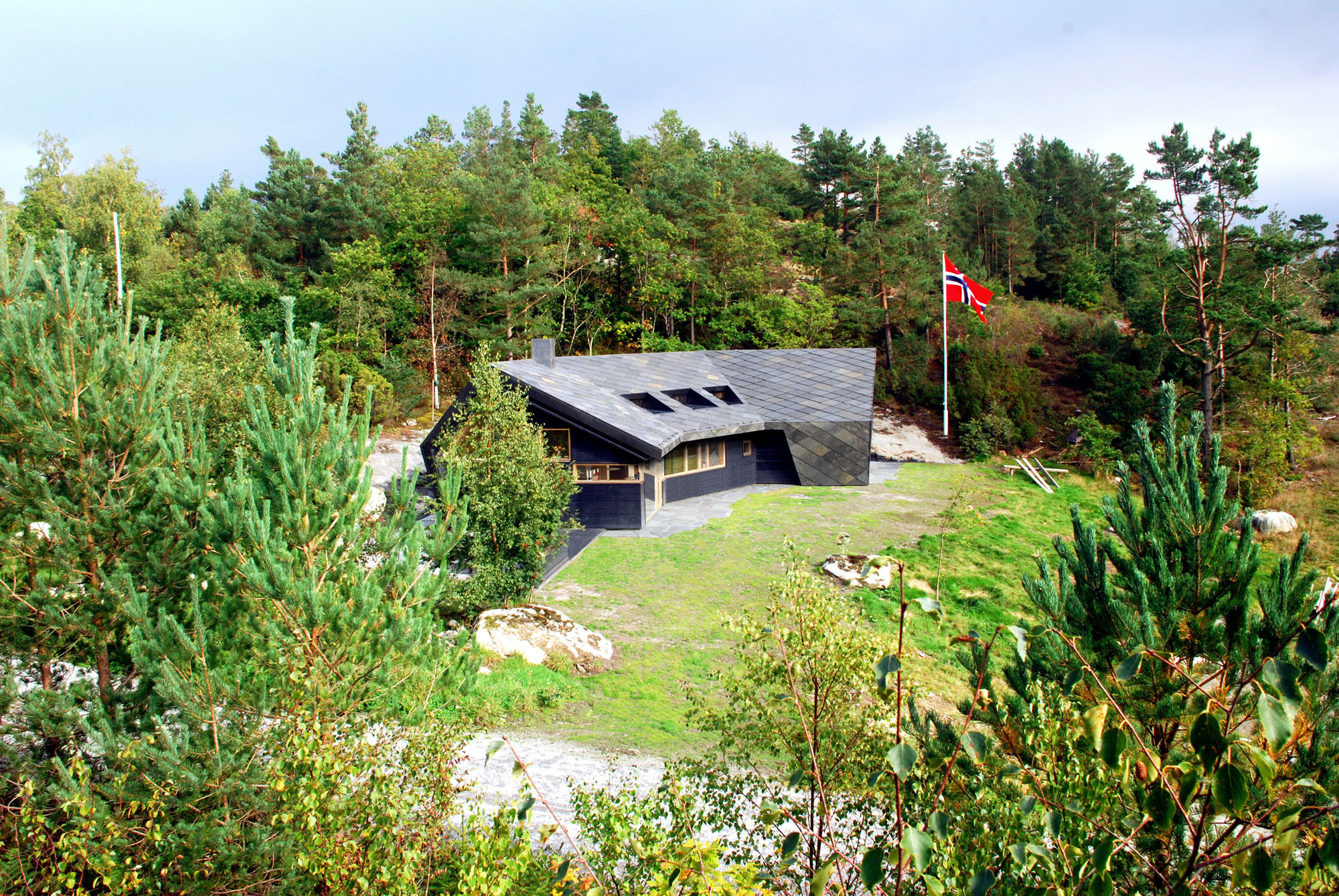Ansicht West: Das zweifach leicht abgewinkelte Gebäude mit asymmetrischem Satteldach schirmt einen Vorplatz vor rauem Nordwind ab