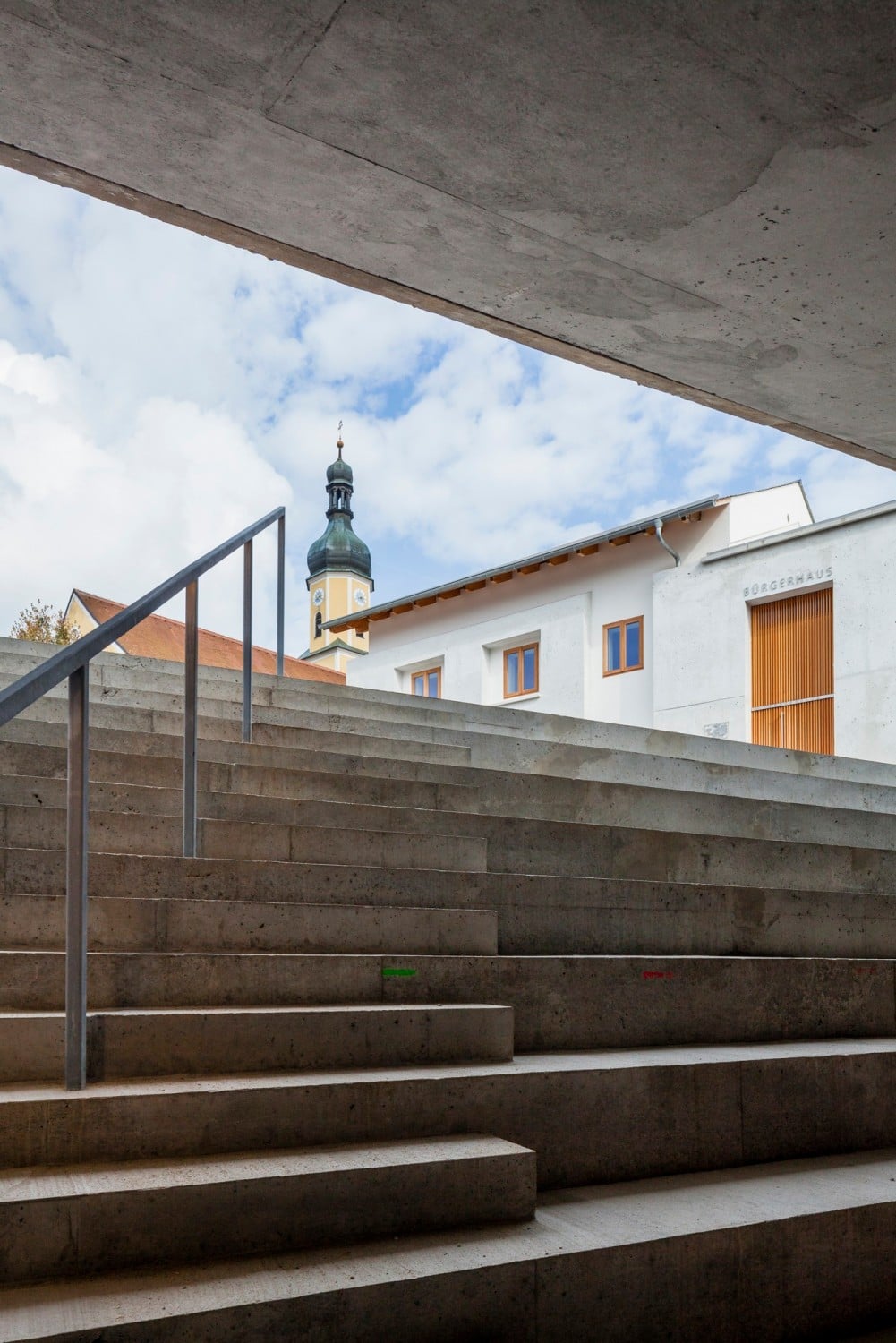 Das Konzerthaus wird vom Dorfplatz aus über eine Freitreppe erschlossen, die unter das quaderförmige Volumen führt