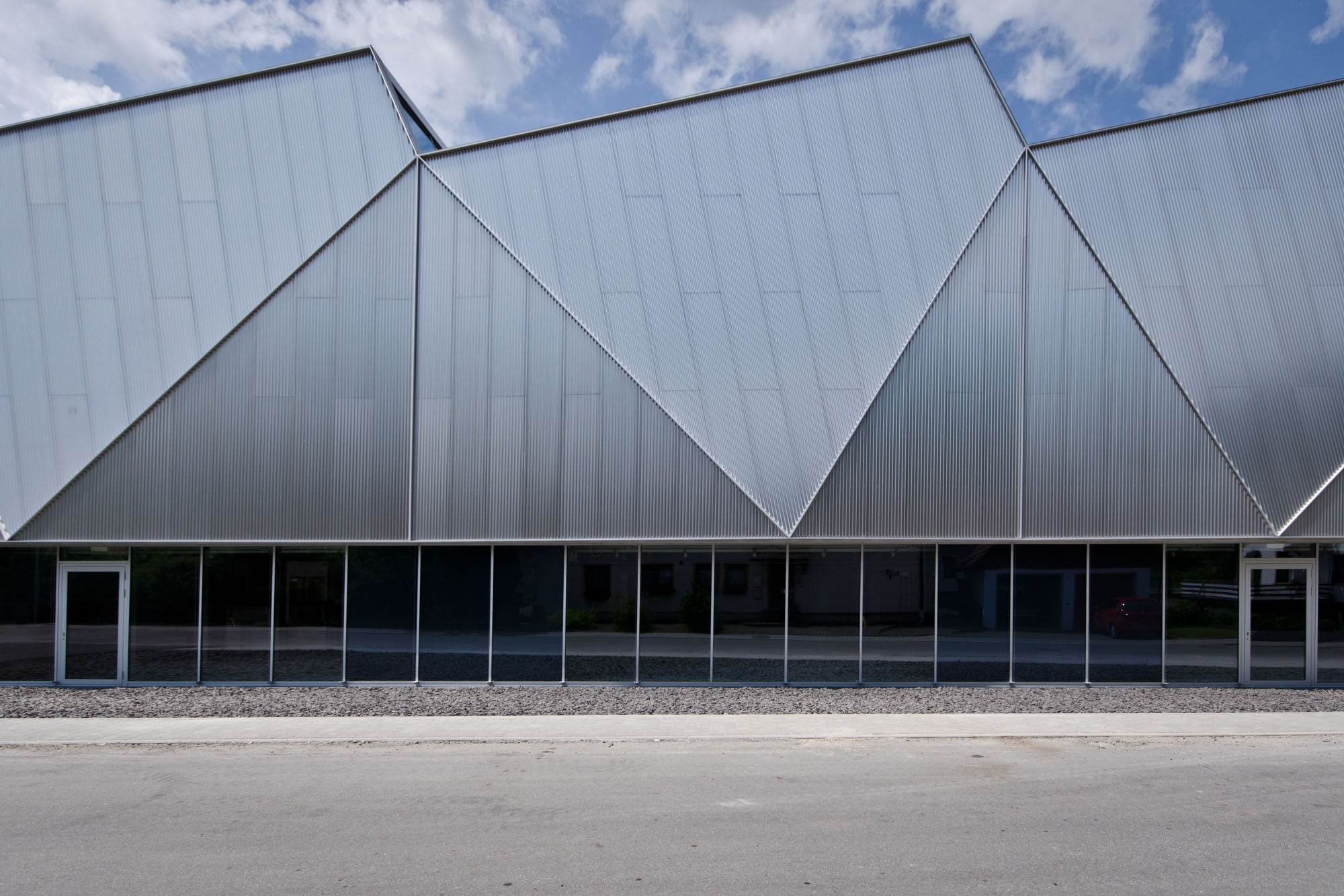Die abgewinkelten Aluminiumflächen umschließen die Hallenseiten oberhalb eines drei Meter hohen Glasbandes und bilden den Übergang zum Sheddach