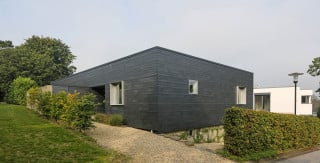 Ansicht Ost von der Straße: Die Fassade ist mit unterschiedlichen rechteckigen Schiefern horizontal gegliedert