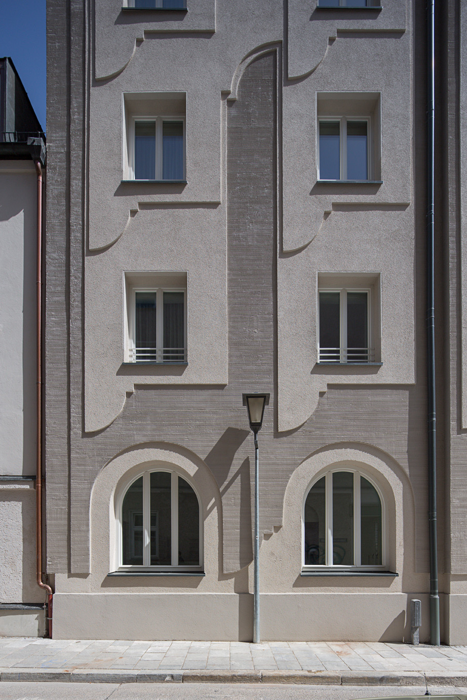 Kamm- und Kratzstruktur wechseln sich ab und gliedern die Fassade; dabei wird das vorgefundene Motiv der Rundbogenfenster modern adaptiert