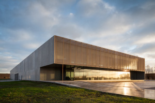 Die Eingangs- und Hauptfassade des Firmensitzes bildet die nach Westen weisende Flanke des zweigeschossigen Büro- und Verwaltungstraktes mit hohen Verglasungen und einer Sonnenschutzverkleidung aus Streckmetall