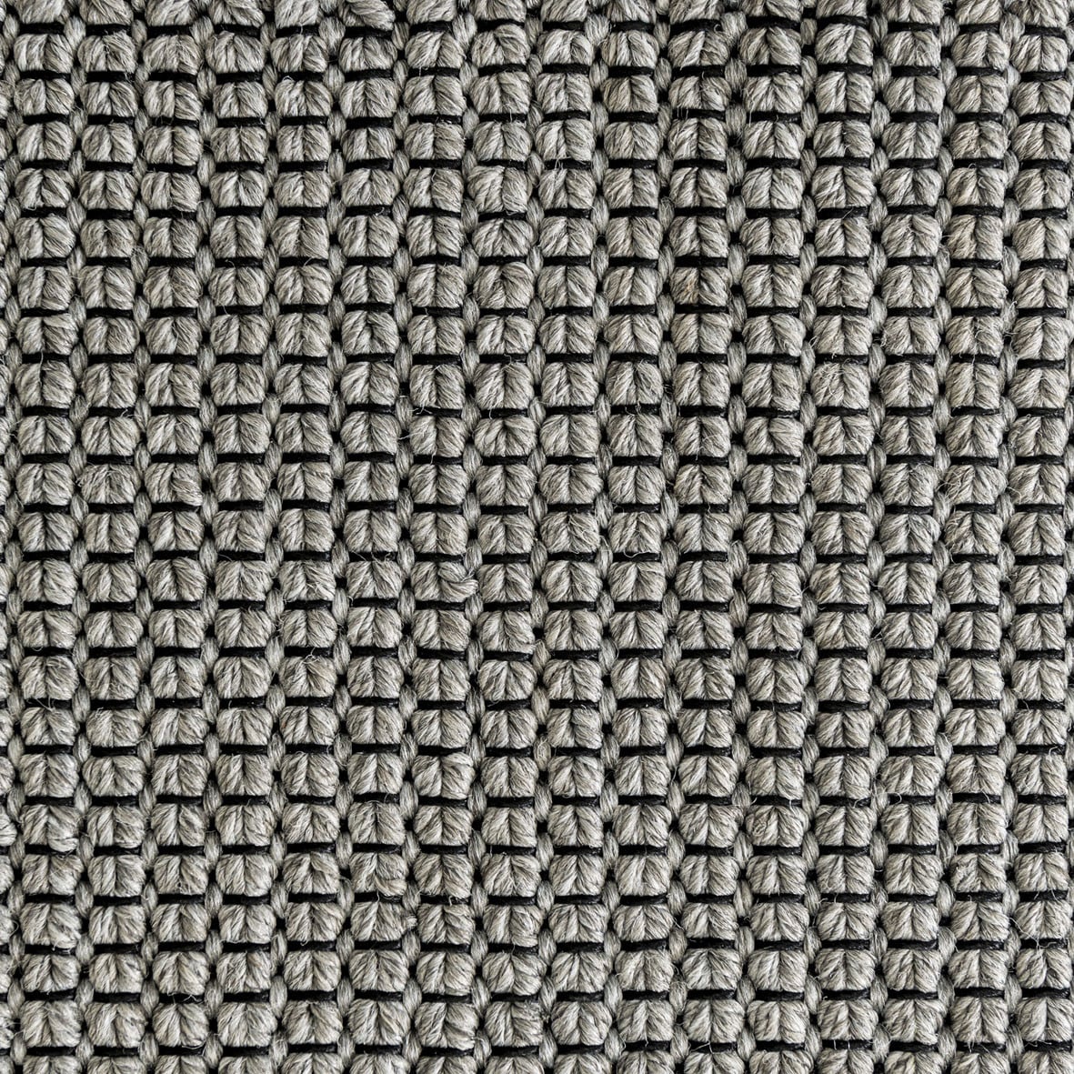 Ein dicht gewebtes, sehr filigranes Zopfmuster durchwirkt von einem kontrastierenden Faden kennzeichnet den Teppich The Grid (Abb. Farbe light grey & black)