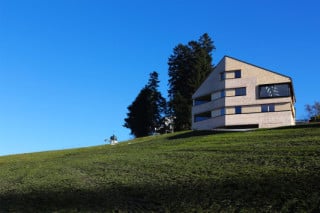 Das Wohnhaus am Hang orientiert sich in Größe, Dachform und Materialität am örtlichen Vorbild des Bregenzerwälderhauses