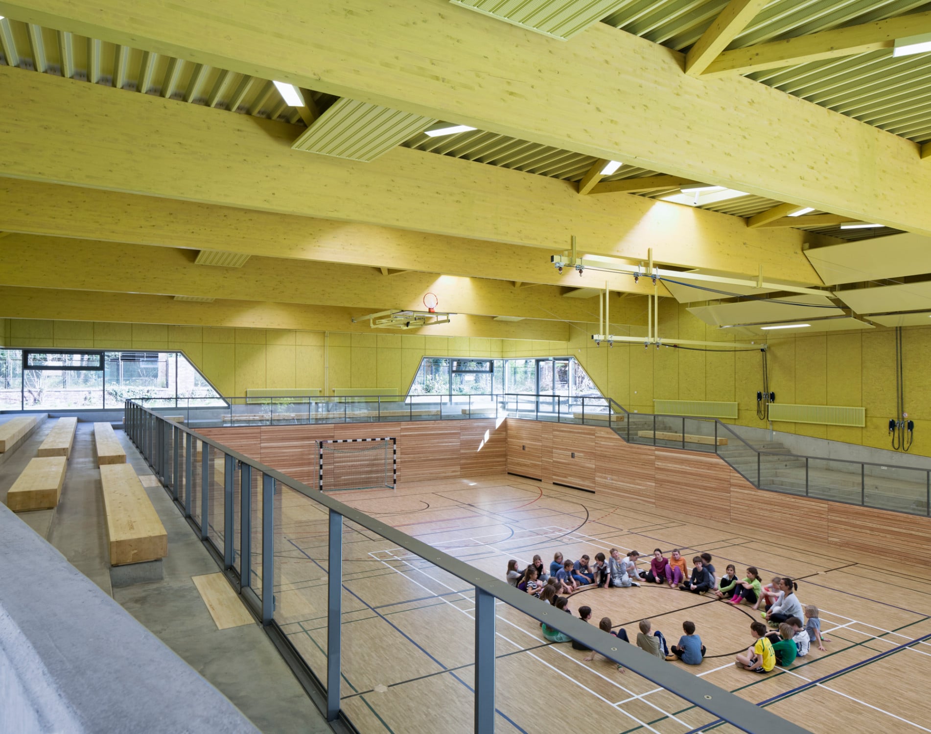 Das Sportfeld ist an drei Seiten von einer Galerie mit treppenartigen Tribünenplätzen aus Sichtbeton und Massivholz umgeben