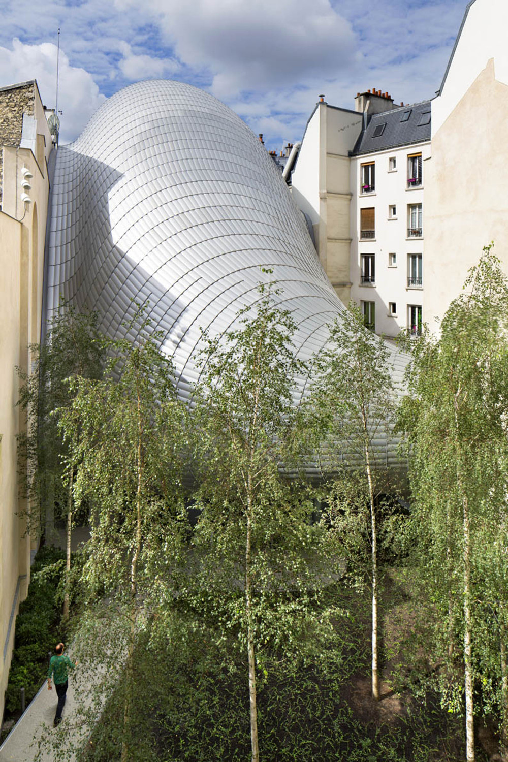 Wie eine gigantische grau-schillernde Raupe quillt der Neubau in den Hof hinein