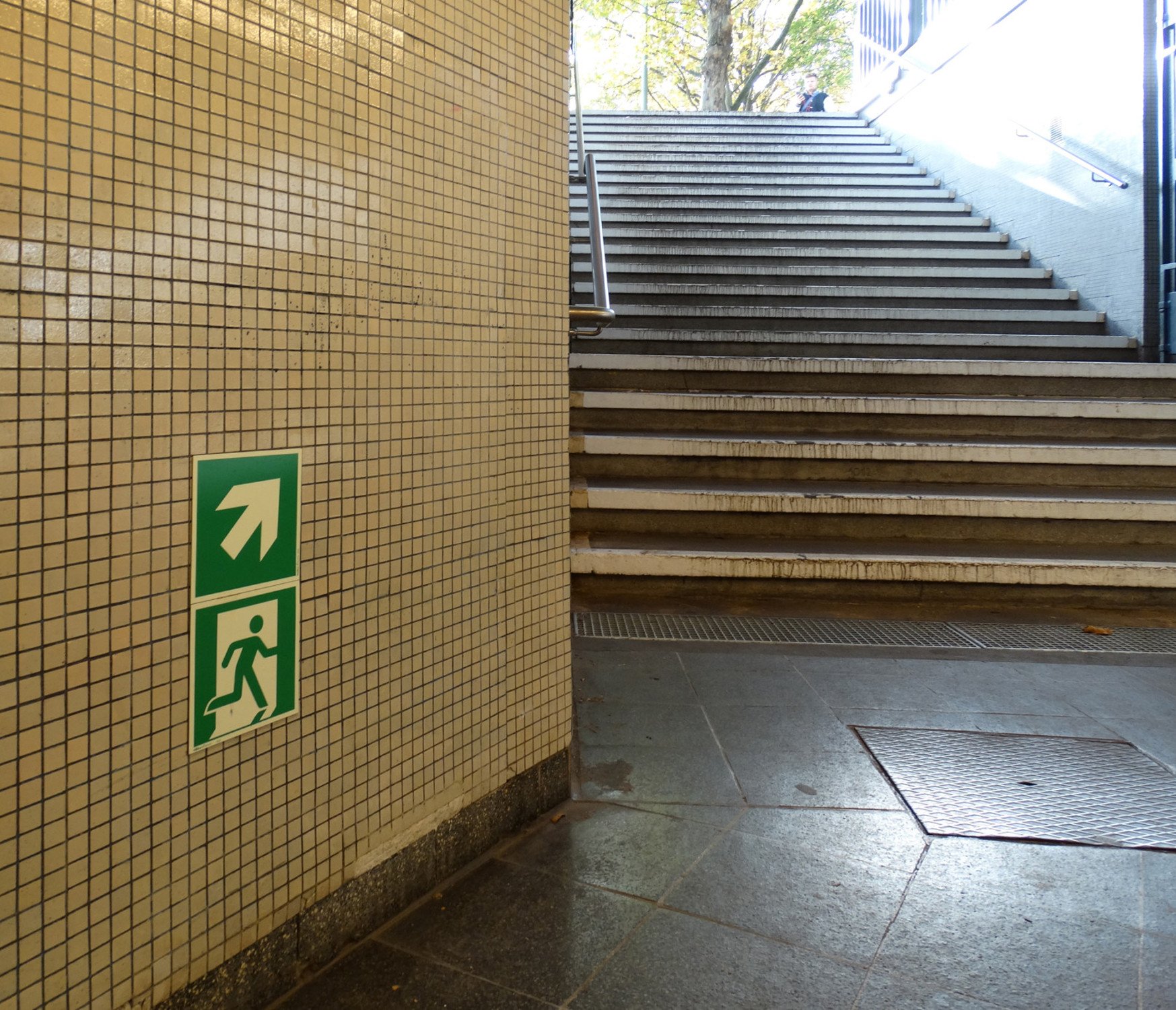 Sicherheitszeichen mit Richtungsangabe nach oben im unteren Bereich der Wand, U-Bahnstation Spichernstraße in Berlin