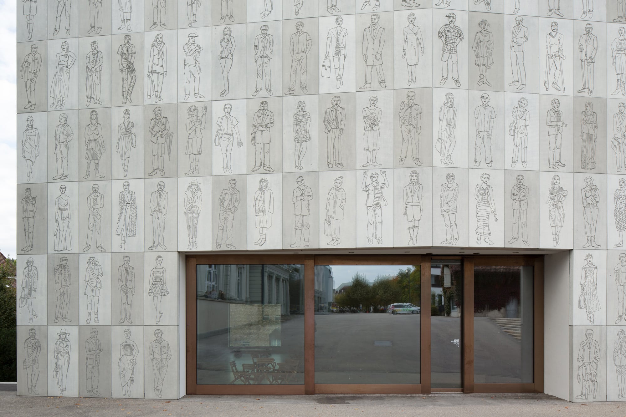 Die fensterlose Betonfassade des Neubaus öffnet sich mit einem scheunentorbreiten Eingang zum Platz